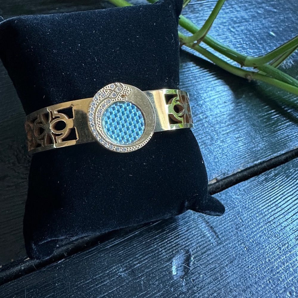 Gold bracelet with detail on cuff, circular blue and rhinestone pendant.